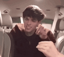 a young man is sitting in the back seat of a car with a hand reaching out towards him .