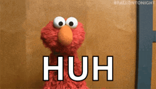 elmo from sesame street is standing in front of a wooden wall with the word huh written on it .