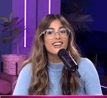 a woman wearing glasses stands in front of a microphone