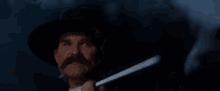 a man with a hat and mustache is holding a gun in his hand and saying `` hell 's coming with me '' .