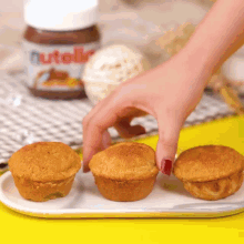 a person reaches for a cupcake on a plate with a jar of nutella behind them