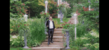 a man in a tuxedo is standing on stairs in a garden .
