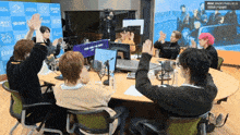 a group of people sitting around a table with their hands in the air in front of a screen that says mbc radio