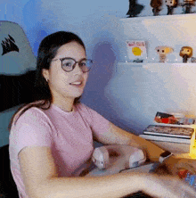 a woman wearing glasses and a pink shirt is sitting at a desk