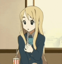 a blonde anime girl is sitting at a table with a cup of popcorn