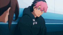 a man with pink hair and a black hoodie looks at another person
