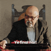 a man in a suit sitting at a desk with ye final hai written on the screen