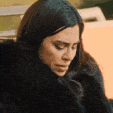 a woman wearing a black fur coat looks down with her eyes closed