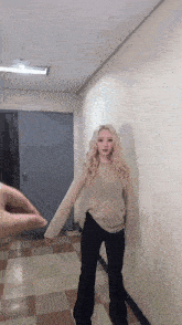 a woman with blonde hair is standing in a hallway wearing a sweater and black pants