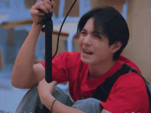 a man in a red shirt is holding a black object in his hands