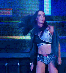 a woman in a crop top and shorts is dancing on a stage in front of a blue background