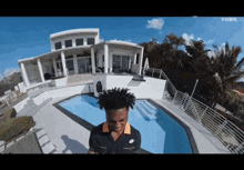 a man stands in front of a swimming pool in front of a large house