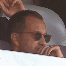 a man wearing sunglasses looks out of a window with his hand on his chin