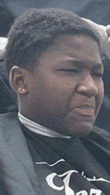 a young man is sitting in a chair with his eyes closed and wearing a black cape .