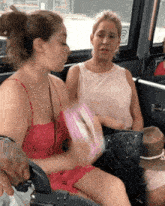 two women are sitting on a bus and one of them is wearing a red top