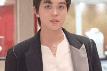 a young man wearing a black jacket and a white shirt is looking at the camera