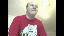 a bald man wearing a red shirt with a polar bear on it is making a funny face .
