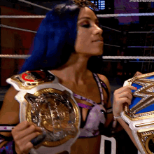 a woman with blue hair is holding a wrestling championship belt in a ring