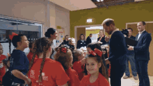 a man in a suit talks to a group of young girls who are wearing red shirts that say " safestart "