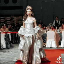 a woman in a white dress is walking down a red carpet with a tiktok logo on the bottom
