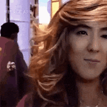 a close up of a woman 's face with long hair and a man walking behind her .