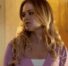 a woman with long blonde hair is wearing a purple sweater and a white shirt .