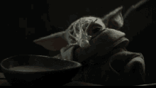 a baby yoda eating from a bowl with his hand in the air