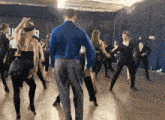 a man in a blue shirt leads a group of dancers in a dance studio