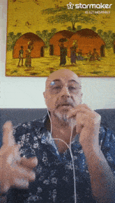 a man wearing ear buds is talking in front of a painting that says starmaker