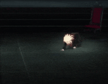 a person is kneeling on the floor in a dark room with a chair .