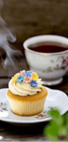 a cupcake with flowers on top is on a plate next to a cup of tea