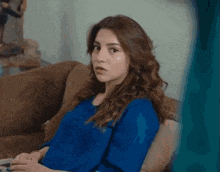 a woman is sitting on a couch wearing a blue shirt and looking at the camera .