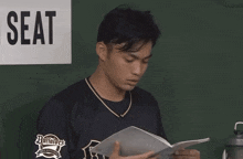 a man reading a book in front of a seat sign