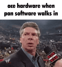 a man in a suit is talking into a microphone with the words ace hardware when pan software walks in .