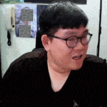 a man wearing glasses is sitting in front of a wall with a picture of a man on it