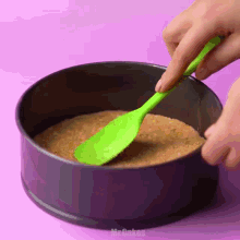 a person is using a green spatula to spread a cake batter in a pan
