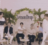 a group of people sit in front of a lemon drop sign