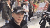 a man wearing a black hat with the letter t on it stands in front of a crowd of people