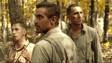 a group of men are standing in the woods looking at something .