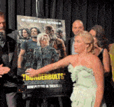 a woman in a green dress stands in front of thunderbolts movie poster