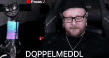 a man wearing glasses and a hat is sitting in front of a microphone with the words doppelmeddl on the screen .