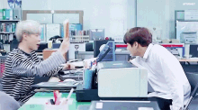two men are sitting at a desk in front of a printer .