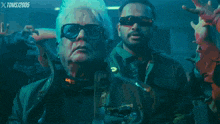 a man wearing sunglasses stands in front of a crowd with the year 2005 on the bottom left