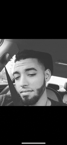 a man with a beard is sitting in a car with a seat belt on .