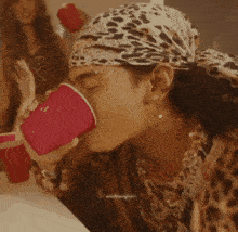 a man wearing a leopard print bandana and holding a pink cup