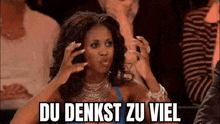 a woman is sitting in a crowd with her hands on her head and a caption that says du denkst zu viel .