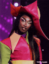 a drag queen is wearing a colorful outfit and hat