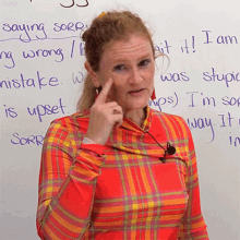 a woman in a plaid shirt stands in front of a white board that says " saying sorry " on it