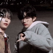 two young men are standing next to each other and one of them is pointing at the camera with his finger .