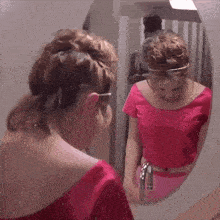 a woman in a pink top looks at her reflection in a mirror